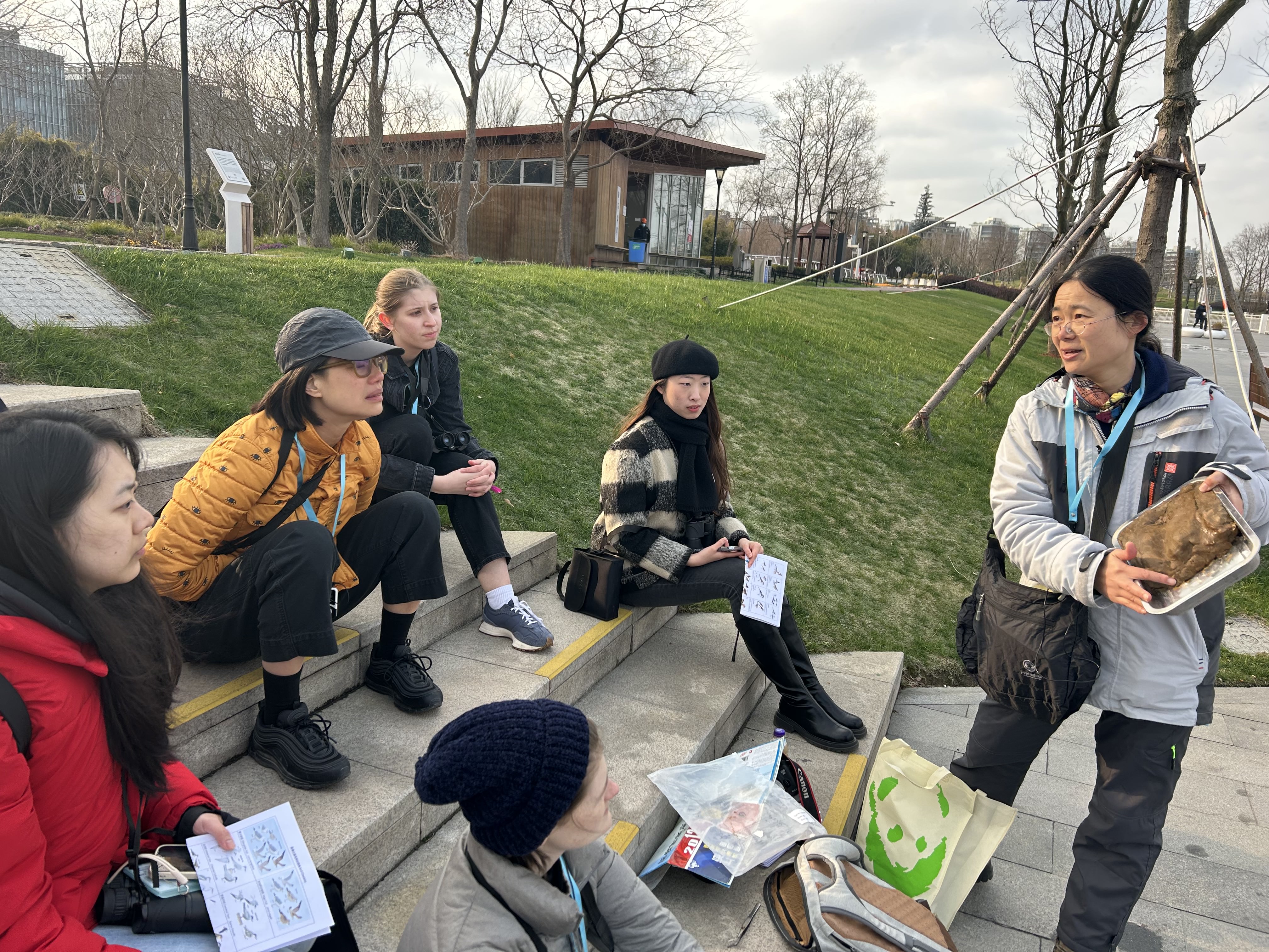 People sitting on steps pay attention to a person explaining the formation of the Huangpu River using a clay model