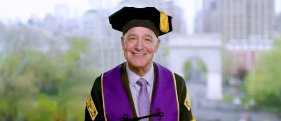 NYU president Andrew Hamilton wearing NYU regalia and giving a speech 